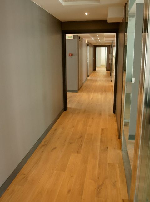 Oak parquet corridor, grey walls, dark frames, glazed partitions on the right.