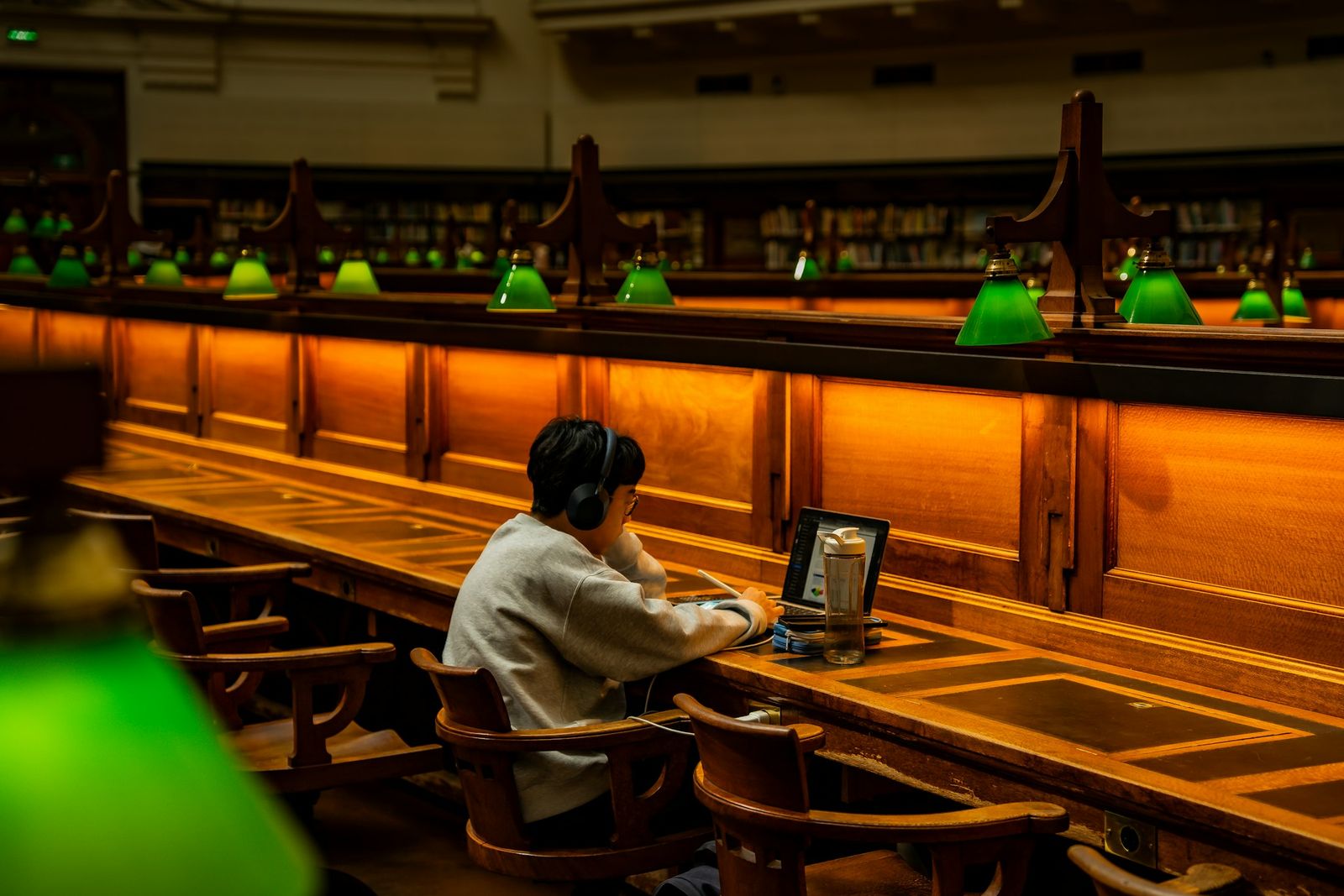 Person concentrating at a long library table lit by lamps.